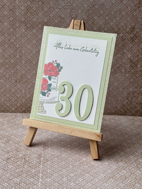 Zu sehen ist eine selbst gebastelte Geburtstagskarte in Lindgrün. Darauf ist auf einem weißen Cardstock eine zweistöckige Torte gestempelt. Die blütenverzierung auf der Torte ist in rot ausgemalt.