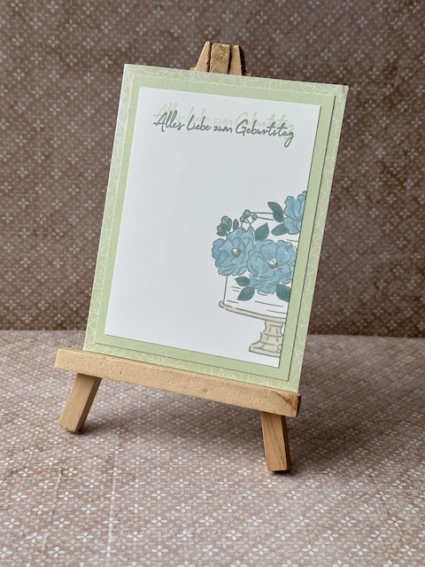 Zu sehen ist eine selbst gebastelte Geburtstagskarte in Lindgrün. Darauf ist auf einem weißen Cardstock eine zweistöckige Torte gestempelt. Die blütenverzierung auf der Torte ist in blau ausgemalt.