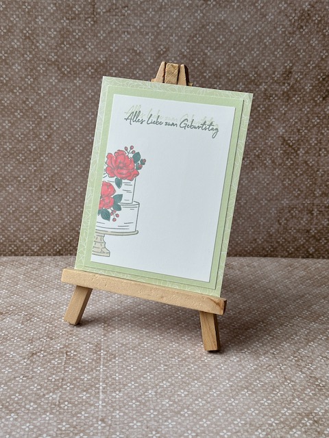 Zu sehen ist eine selbst gebastelte Geburtstagskarte in Lindgrün. Darauf ist auf einem weißen Cardstock eine zweistöckige Torte gestempelt. Die blütenverzierung auf der Torte ist in rot ausgemalt.