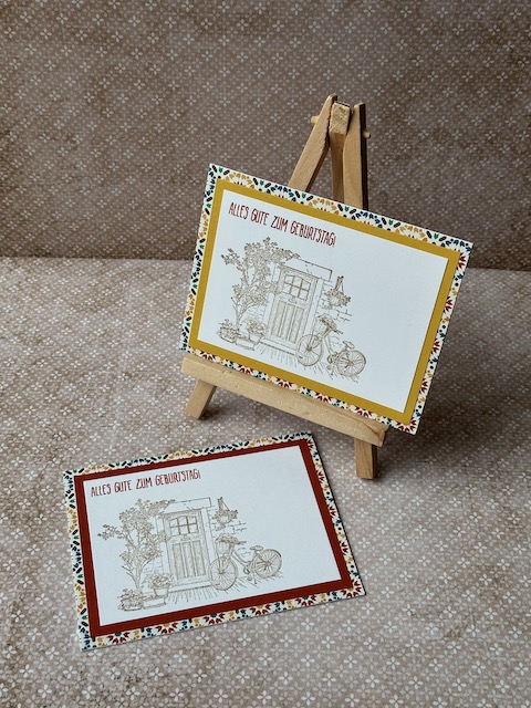 Zu sehen ist eine gebastelte Geburtstagskarte. Vorne drauf ist eine Tür samt dekorierten Rahmen und angelehntem Fahrrad zu sehen. Oben drüber steht: Alles gute zum Geburtstag. Hinterlegt ist das ganze durch einen Farbspiegel und Mosaik Designpapier.