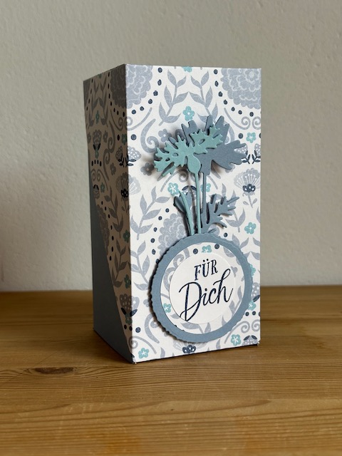 Zu sehen ist eine selbstgemachte Verpackung, die PLatz bietet für eine Prosecco Dose. Die Grundform ist ein Quader, wobei der Deckel Diagonal über die Schachtel geklappt wird und so raffiniert aussieht.