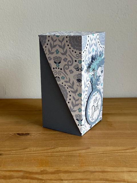 Zu sehen ist eine selbstgemachte Verpackung, die PLatz bietet für eine Prosecco Dose. Die Grundform ist ein Quader, wobei der Deckel Diagonal über die Schachtel geklappt wird und so raffiniert aussieht. 