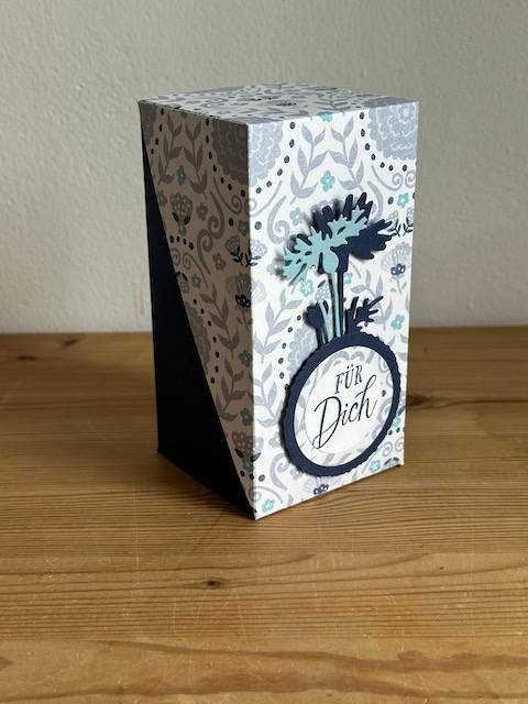Zu sehen ist eine selbstgemachte Verpackung, die PLatz bietet für eine Prosecco Dose. Die Grundform ist ein Quader, wobei der Deckel Diagonal über die Schachtel geklappt wird und so raffiniert aussieht. 