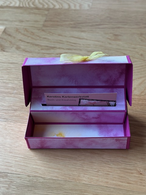 Zu sehen ist eine selbstgebastelte Box, die man aufklappen kann. Sichtbar wird ein Schlitz, in den eine Gutscheinkarte gesteckt werden kann. In der Box ist außerdem noch PLatz für etwas süßes zum Beispiel drei bis vier kleine Schokoladenkugeln