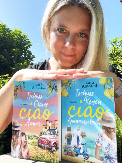 Ein Foto der Autorin Lara Amorelli mit zwei ihrer Bücher vor sich.