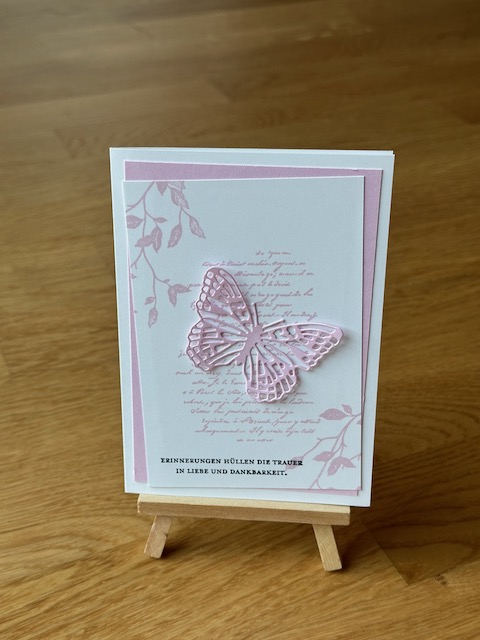 Zu sehen ist eine selbstgebastelte Trauerkarte. Allerdings nicht in klassischem schwarz weiß. Auf der weißen Grundkarte klebt ein rosa Layer und darauf ein weitere in weiß. Dieser ist mit rosa bestempelt. Darüber wurde ein rosa Schmetterling geklebt. Einzig die Beileidswünsche sind in schwarz gestempelt.