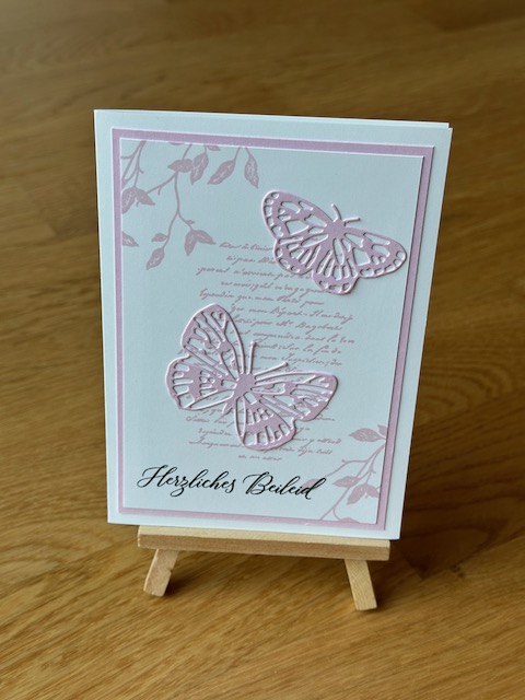 Zu sehen ist eine selbstgebastelte Trauerkarte. Allerdings nicht in klassischem schwarz weiß. Auf der weißen Grundkarte klebt ein rosa Layer und darauf ein weitere in weiß. Dieser ist mit rosa bestempelt. Darüber wurde ein rosa Schmetterling geklebt. Einzig die Beileidswünsche sind in schwarz gestempelt.