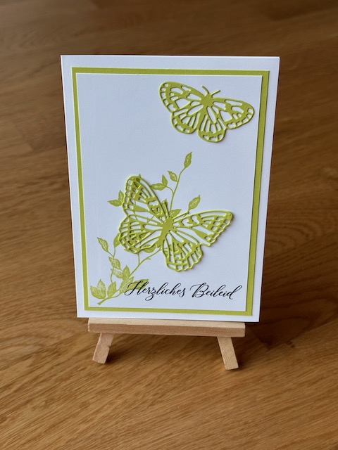 Zu sehen ist eine selbstgebastelte Trauerkarte. Allerdings nicht in klassischem schwarz weiß. Auf der weißen Grundkarte klebt ein grün Layer und darauf ein weitere in weiß. Dieser ist mit grün bestempelt. Darüber wurde ein grüner Schmetterling geklebt. Einzig die Beileidswünsche sind in schwarz gestempelt.