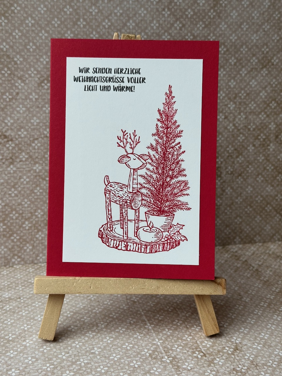Zu sehen ist eine selbstgebastelte Weihnachtskarte in Rot und weiß. Aufgestempelt ist ein lieber Gruß zu Weihnachten und ein Motiv mit einem Holzreh, einem Weihnachtsbaum und einem Apfel aus dem Stempelset: RUSTIC CENTERPIECE von Stampin Up