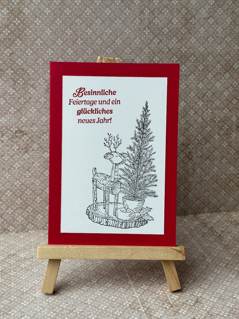 Zu sehen ist eine selbstgebastelte Weihnachtskarte in Rot und weiß. Aufgestempelt ist ein lieber Gruß zu Weihnachten und ein Motiv mit einem Holzreh, einem Weihnachtsbaum und einem Apfel aus dem Stempelset: RUSTIC CENTERPIECE von Stampin Up