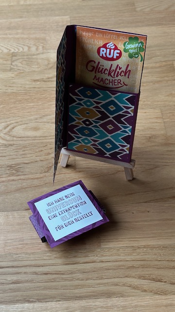 Kleine selbstgemachte Verpackung um einen Tassen Pudding zu verschenken. Auf der Verpackung steht: Ich habe beim Universum eine extra Portion Glück für dich bestellt.