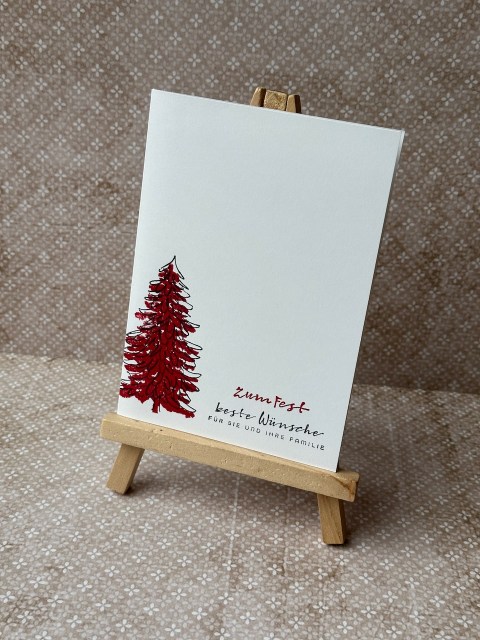 Zu sehen ist eine ganz schlichte Weihnachtskarte. Die Grundkarte ist weiß und darauf wurde in zwei Lagen ein Tannenbaum in schwarz und rot gestempelt. Passend dazu ist der Spruch: Zum Fest beste Wünsche für sie und ihre Familie auch in rot und schwarz gestempelt.