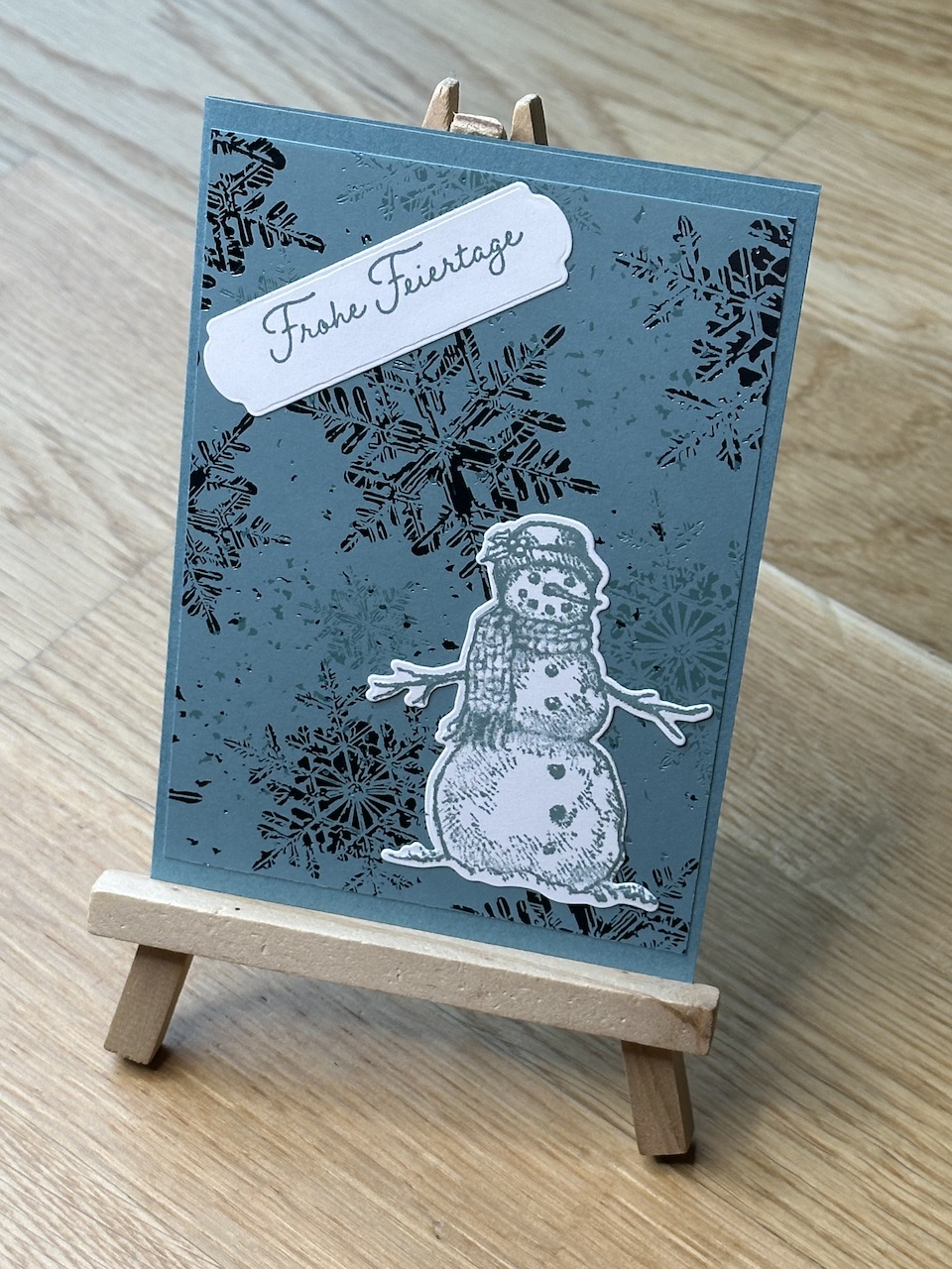 Selbstgebastelte Weihnachtskarten mit metallischen Akzenten auf Papier. In blau, orange und rot. Jeweils mit Schneemann oder Stern und einem besonderen Glitzern, wenn man die Karte im Licht bewegt.