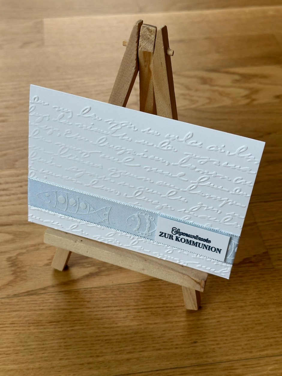 Selbstgebastelte Karte zur Kommunion in weiß mit hellblauem Band und Prägung