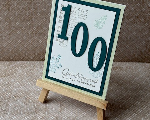 Gebastelte Geburtstagskarte mit mittgrüner Grundkarte und Smaragd-Layer, weißer Deckseite mit Eckstempel, grünen Blüten und Blättern am Rand, Variante mit Zahlen 70 und 100, handgefertigtes Unikat.